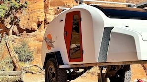 Un camping-car blanc est garé dans un désert, avec des formations rocheuses rouges en arrière-plan.