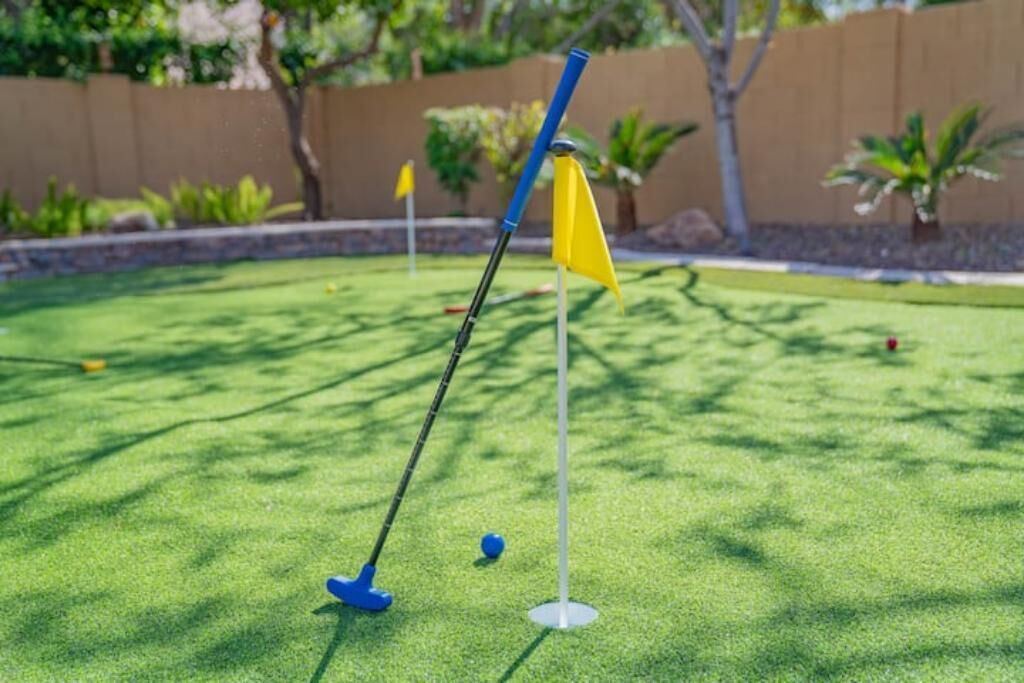 A miniature golf course with a green artificial turf, a blue golf club, and a yellow flag.