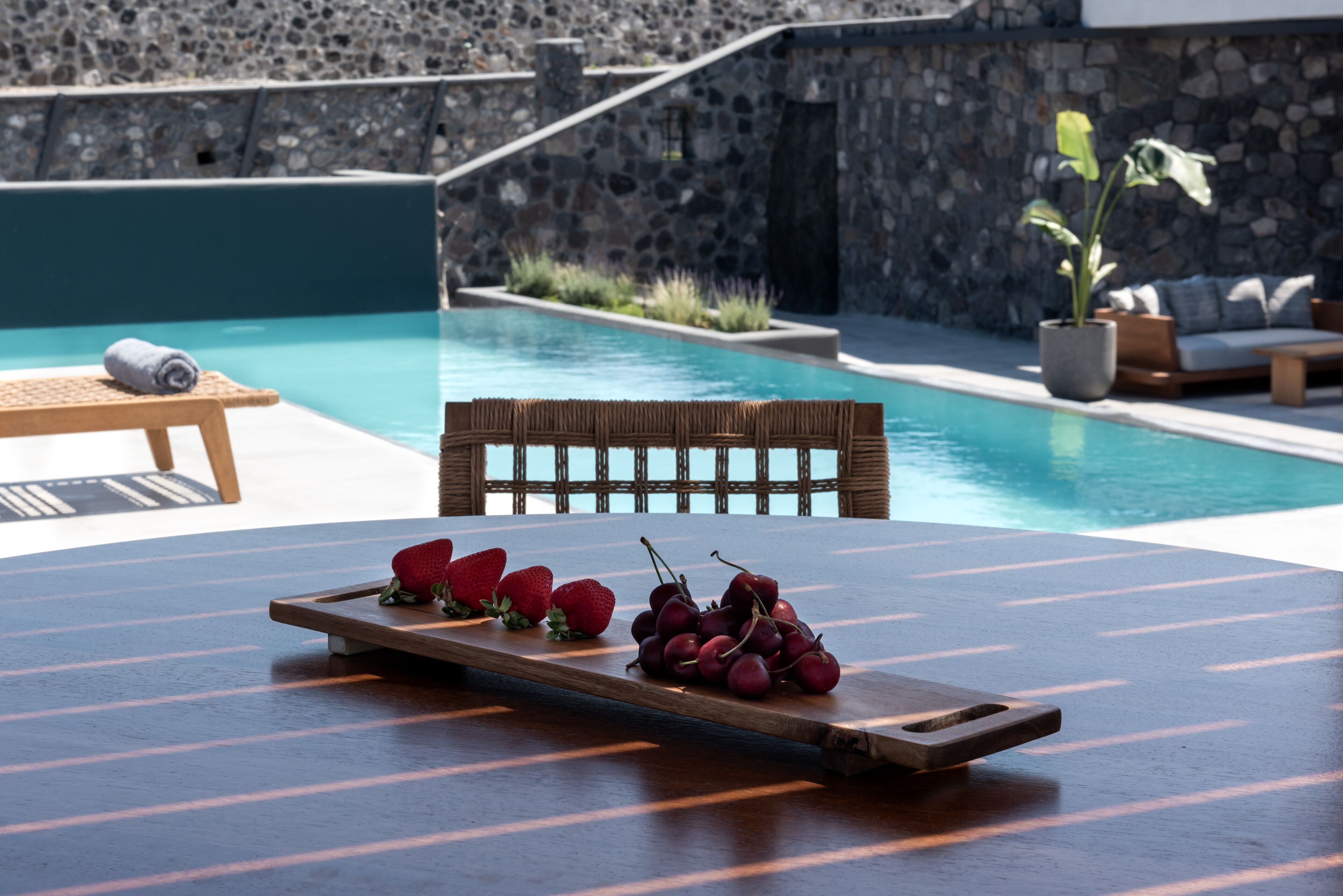 A poolside area with a wooden table, a wicker chair, and a bench.