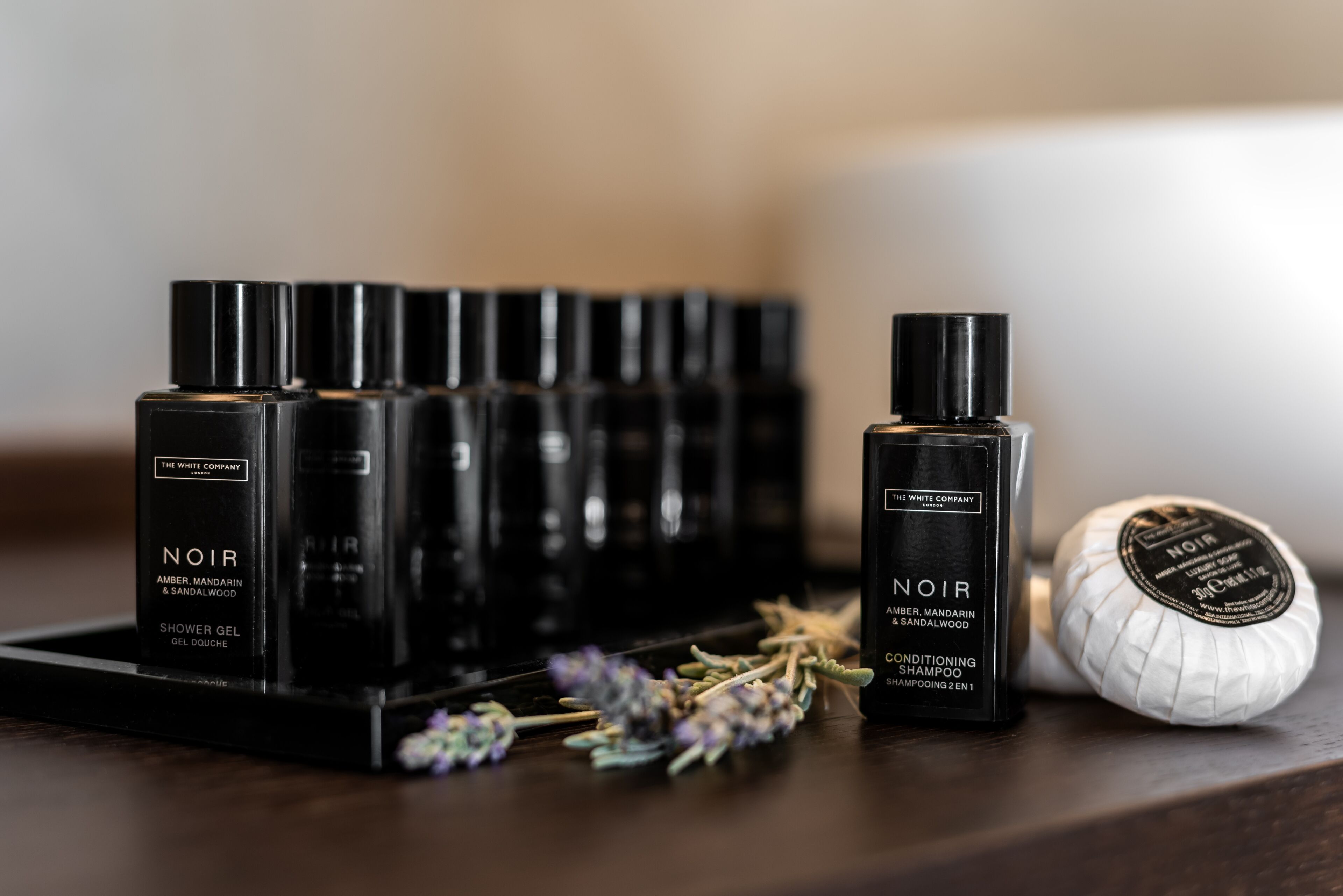 Mehrere schwarze Flaschen mit dem Aufdruck 'NOIR', die verschiedene Anwendungen wie Duschgel und Shampoo haben, zusammen mit einer weißen Seife.