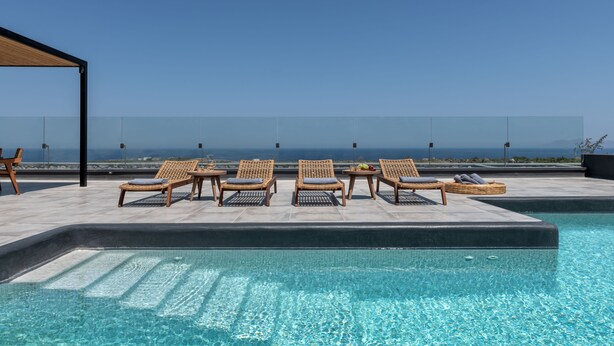 A rooftop pool area with lounge chairs and a clear view of the ocean.