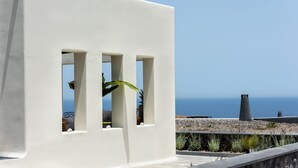 A white building with three rectangular windows and a view of the sea.
