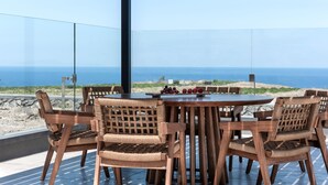A wooden dining table with chairs, a glass railing, and a view of the ocean.