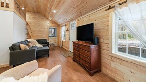 Interior de una cabaña de madera con sofá, televisión y cómoda de madera.