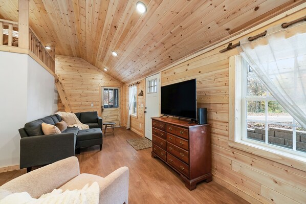 Interior de una cabaña de madera con sofá, televisión y cómoda de madera.