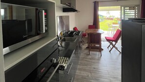 A modern kitchen with a built-in microwave, stove, and sink. There is a dining area with a table and chairs, and a view of the outdoors. - Ânani - Mirimiri Lodge (Raiatea)