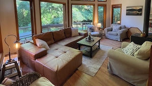 A spacious living room with large windows, a wooden ceiling, and a cozy seating area with sofas and a coffee table.