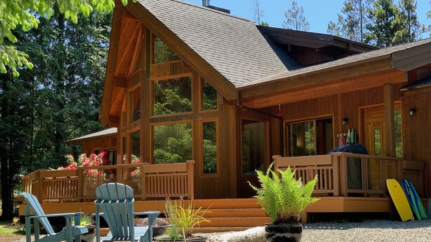 A wooden cabin with large windows, a porch, and outdoor seating.