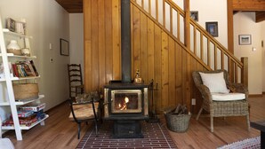 A cozy room with a wood-burning stove, a wicker chair, a bookshelf, and a staircase.