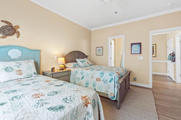 A bedroom with two beds, a nightstand with a lamp, a wall-mounted turtle decoration, and a door leading to another room.