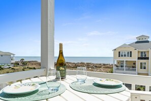 A balcony with a table set for two, overlooking a beach and a house.