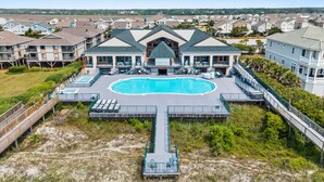 Un resort con una amplia piscina central, varias construcciones y un paseo marítimo que conduce al área de la piscina.