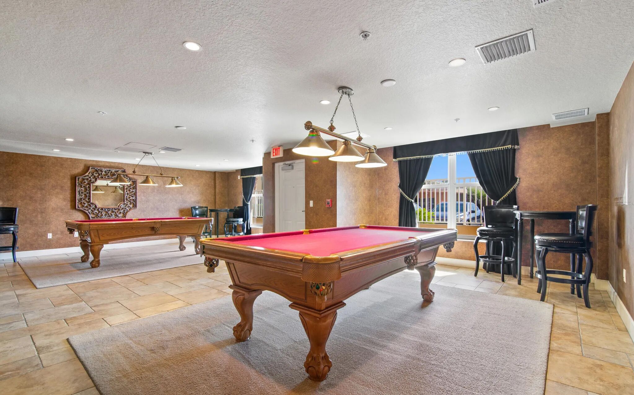 A pool table with a red felt top, a mirror with an ornate frame, and a chandelier.