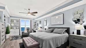 Un dormitorio con una cama grande, ventilador de techo, escritorio y vista al océano.