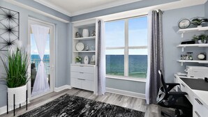 Habitación con vista al mar, un escritorio con una silla y estantes con objetos decorativos.