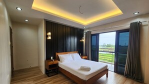 Ein modernes Hotelzimmer mit Holzboden, einem großen Bett mit weißen Leinentextilien, einem Nachttisch und Blick auf eine grüne Landschaft durch eine Glastür.