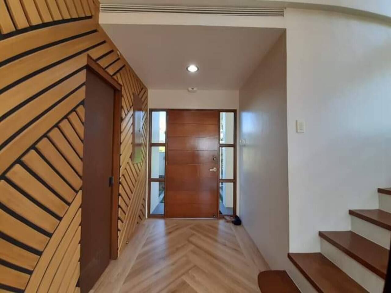 A hallway with a wooden door, a staircase, and a herringbone-patterned wall.