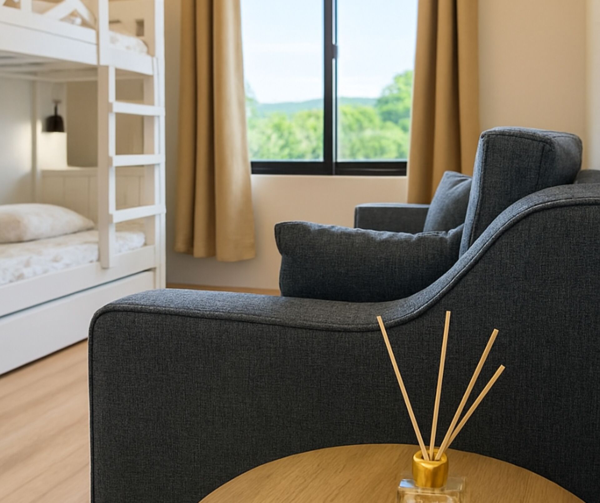 Una habitación moderna con un sofá gris, una mesa de madera con difusor de aroma de junco, y una cama nido al fondo.