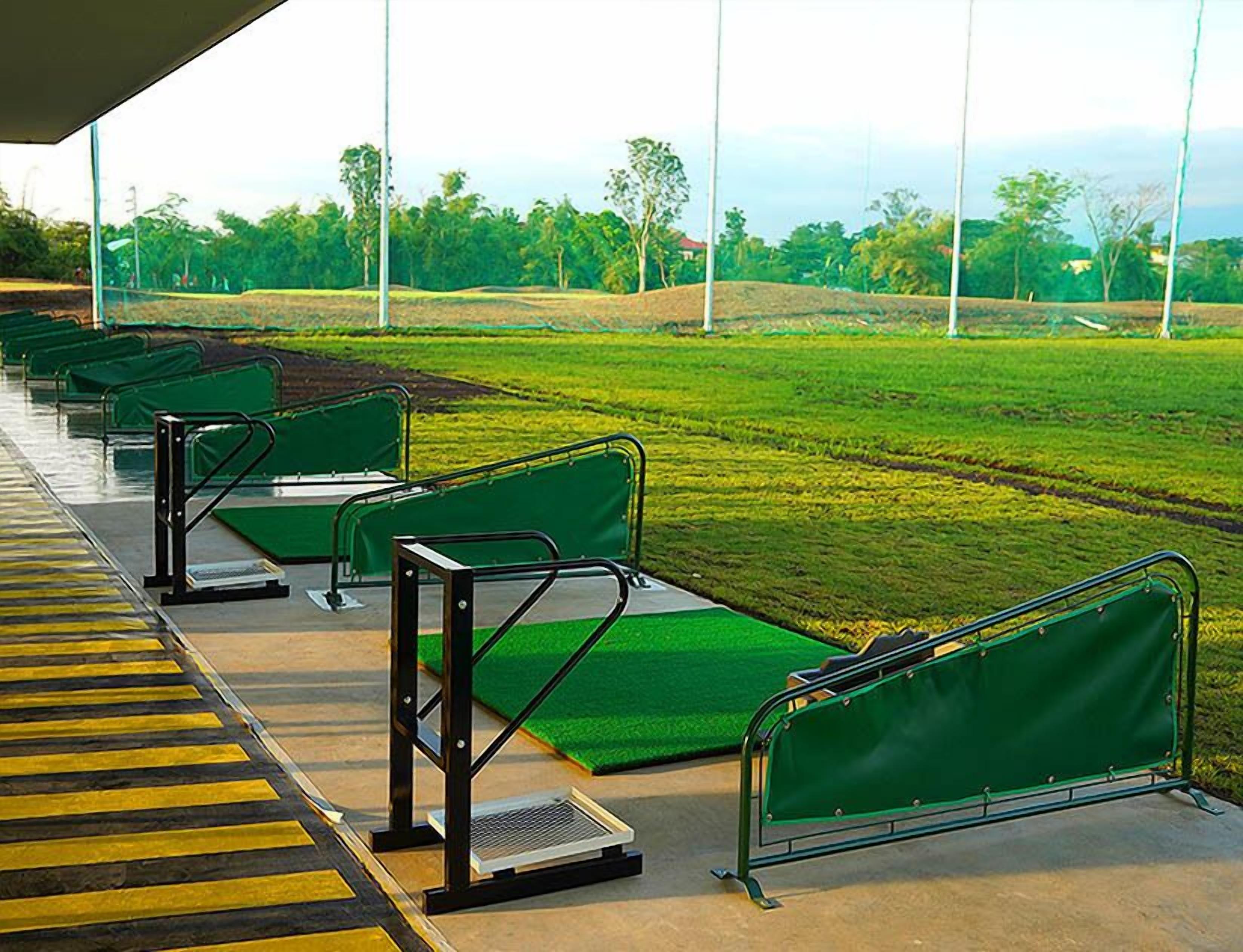 A row of green seating areas with metal railings, a grassy field in the background, and a clear sky.