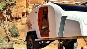 Un camping-car blanc est garé dans un désert, avec des formations rocheuses rouges en arrière-plan.