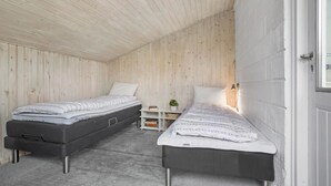 A small, compact room with two single beds, a small table with a lamp, and a white door.