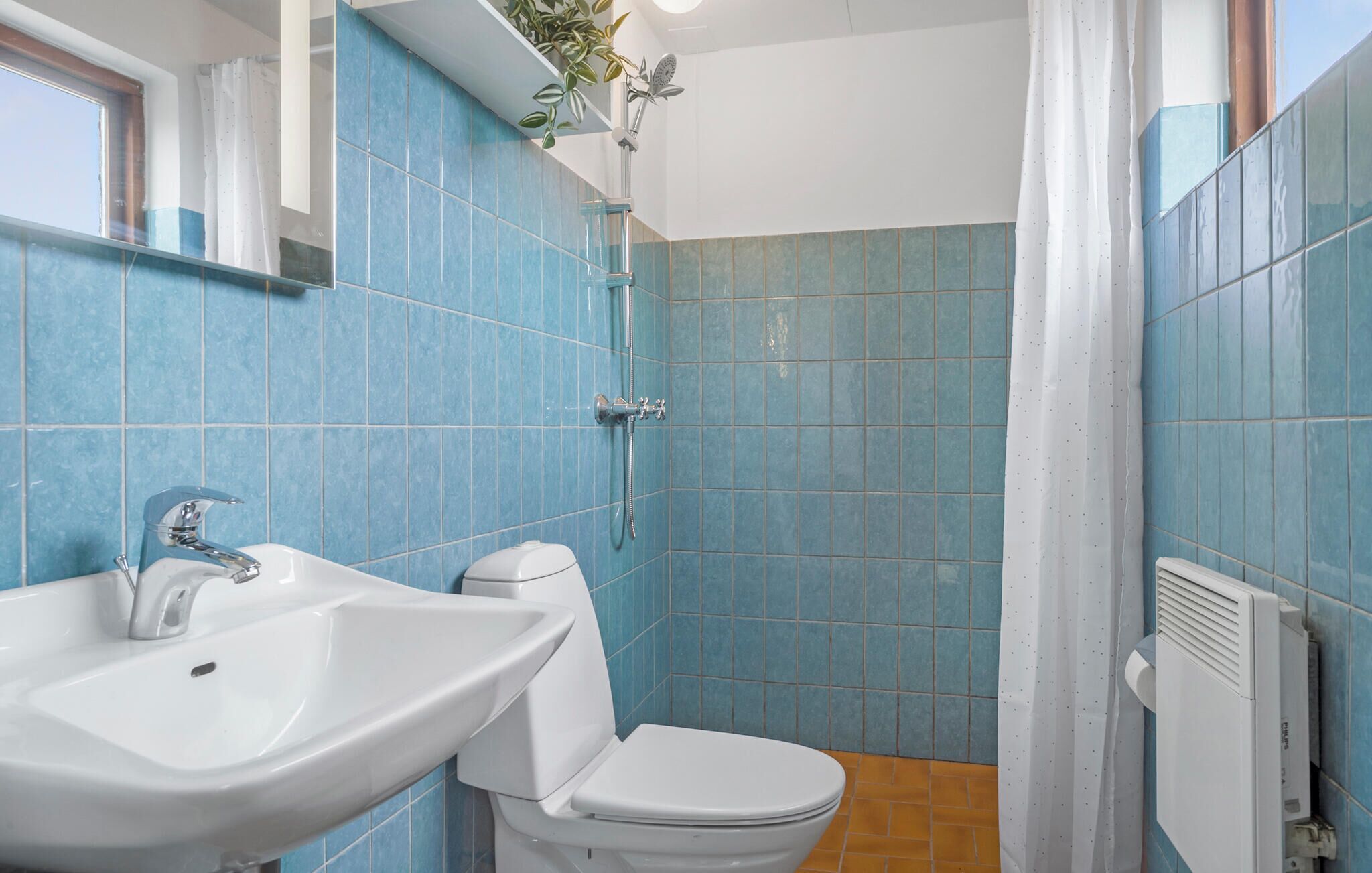 A bathroom with a sink, toilet, shower, and a radiator.