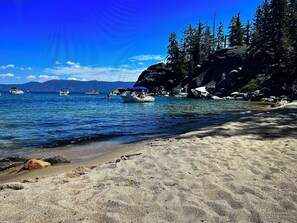 A beach with clear blue water, boats, and a rocky shoreline.