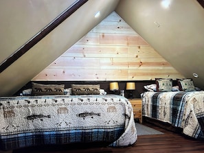 A cozy attic bedroom with two beds, wooden slats on the ceiling, and a view of the sky.