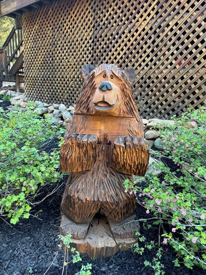 Una escultura de madera de un oso en un jardín, con una cerca de celosía de madera al fondo.