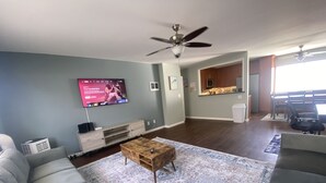 Una sala de estar con un televisor de pantalla plana, un ventilador de techo, una mesa de centro de madera y una alfombra estampada.