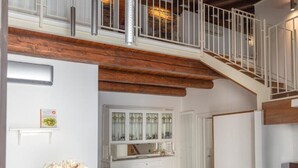Una habitación amplia con una escalera de madera, un armario blanco con puertas de cristal y una mesa de madera con un florero.