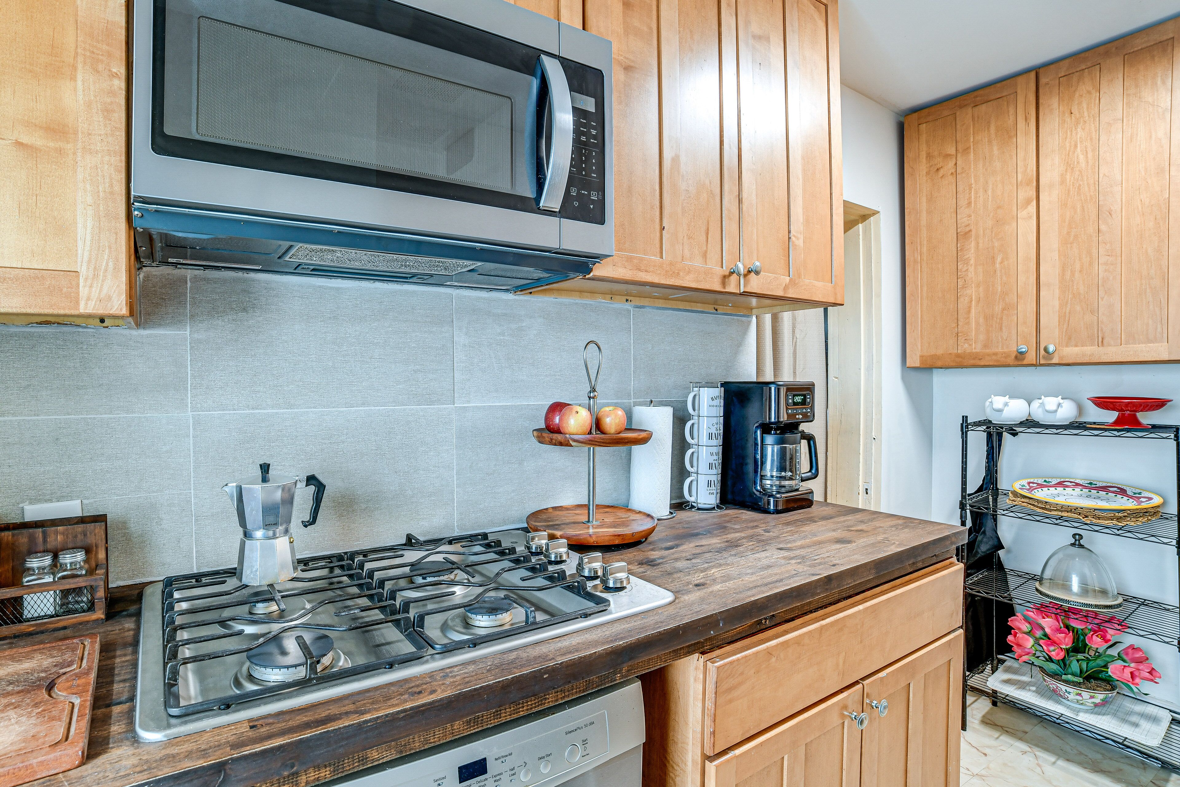 A kitchen with a gas stove, a microwave, wooden cabinets, and a coffee maker.