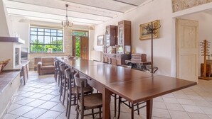 A spacious kitchen with a long wooden table, bar stools, and a built-in oven. - Villa Anna in Monferrato (Rosignano Monferrato)