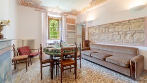 A dining area with a table set for two, a sofa, and a stone wall. - Villa Anna in Monferrato (Rosignano Monferrato)