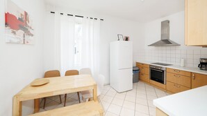 A compact kitchen with a dining area, white tiled walls, a refrigerator, a stove, and a sink.