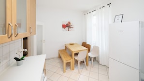 A modern kitchen with white cabinets, a wooden dining table, and a white refrigerator.