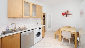 A compact kitchen with wooden cabinets, a washing machine, a sink, and a small dining area with a table and chairs.