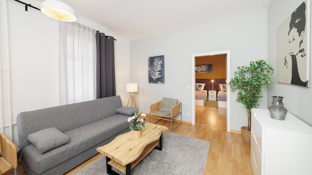 A modern living room with a grey sofa, a wooden coffee table, a wicker chair, and a potted plant.
