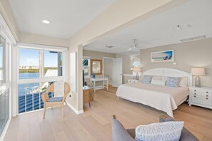A spacious bedroom with a large bed, a desk, and a chair. There is a balcony with a view of the water. - Siesta Bayside With Bay/dock Views (Siesta Key)