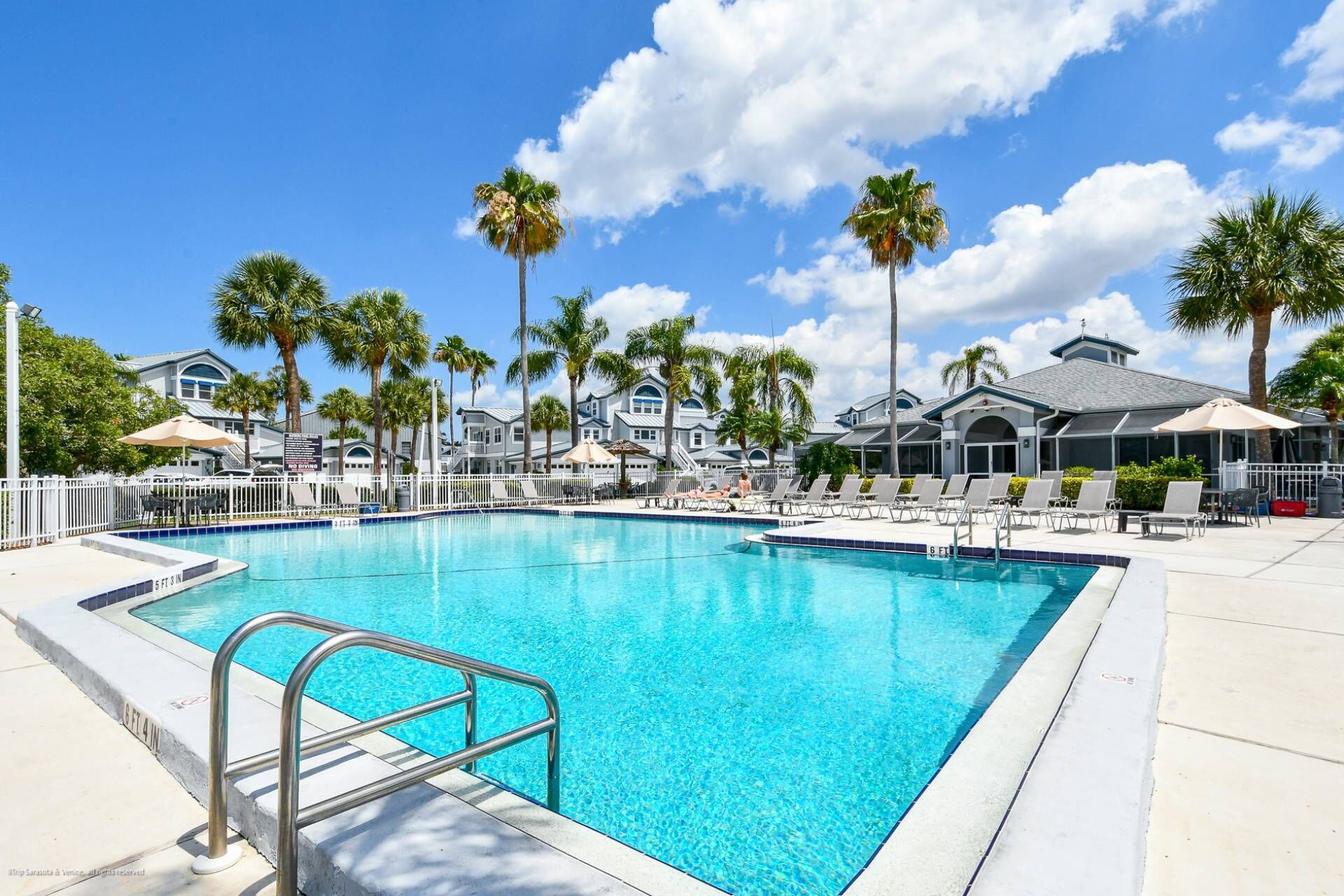 Une piscine à l’eau d’un bleu cristallin, entourée de palmiers et de chaises longues.