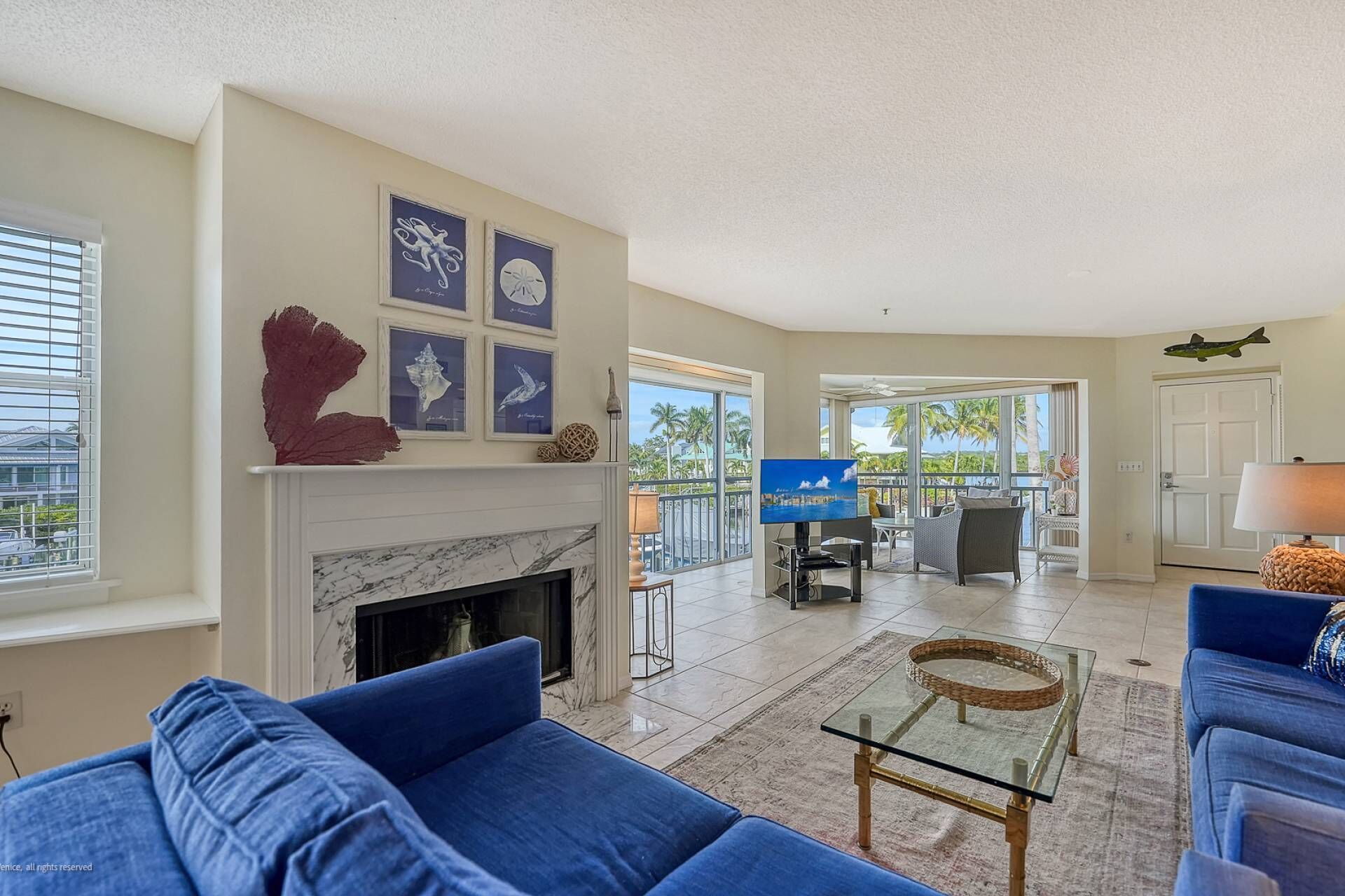 A spacious living room with a fireplace, blue sofas, a glass coffee table, and framed artwork on the wall.