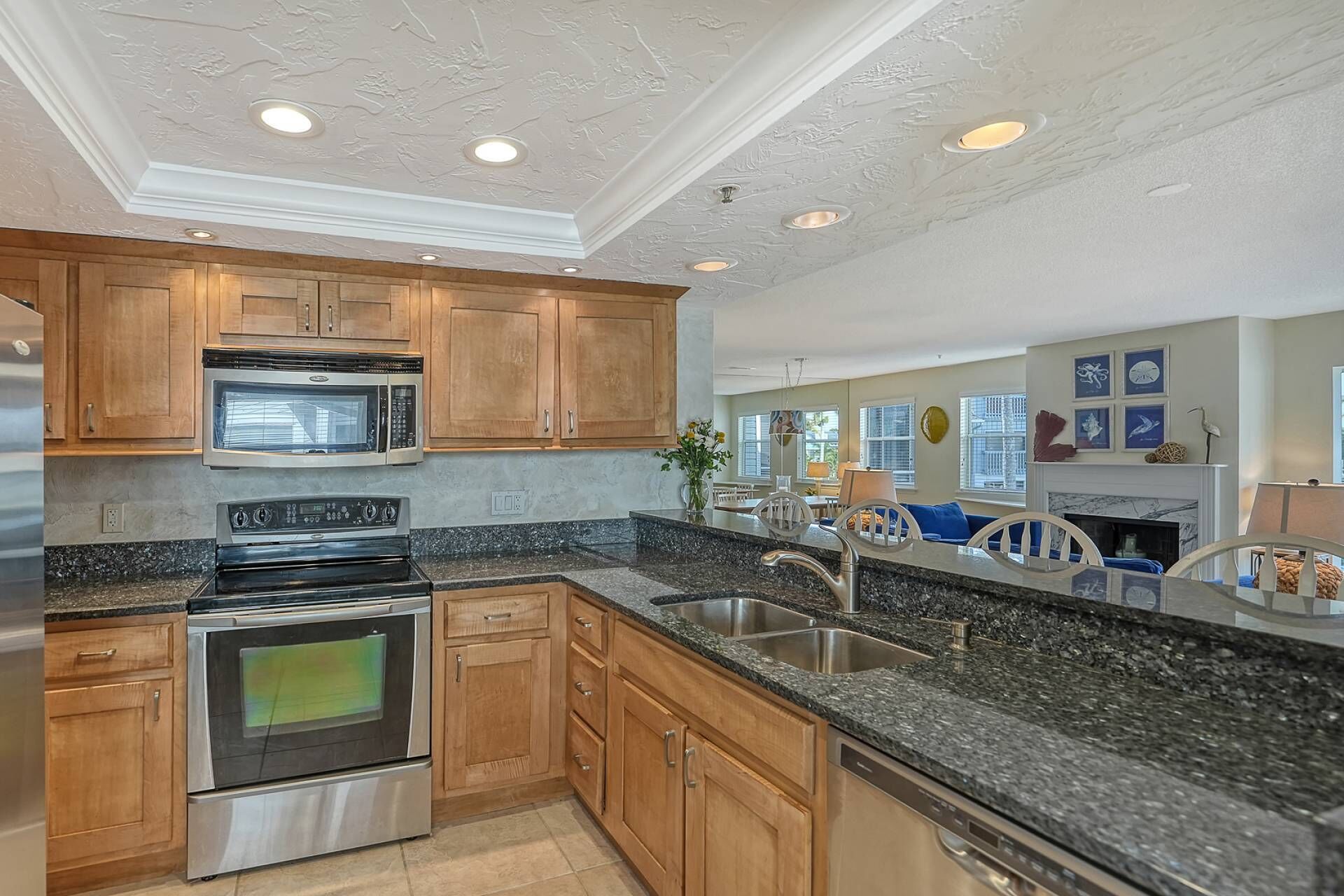 A modern kitchen with wooden cabinets, stainless steel appliances, granite countertops, and recessed ceiling lights.