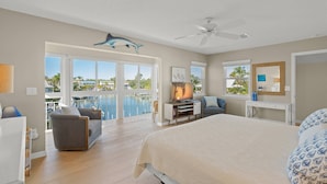 A bedroom with a bed, a desk, a chair, a TV, and a balcony with a view of the sea. - Siesta Bayside With Bay/dock Views (Siesta Key)