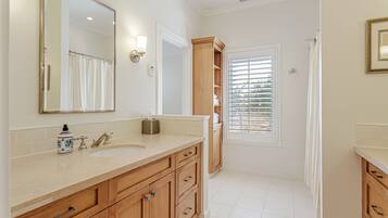 A bathroom with a large mirror, two sinks, wooden cabinets, and a window with blinds.