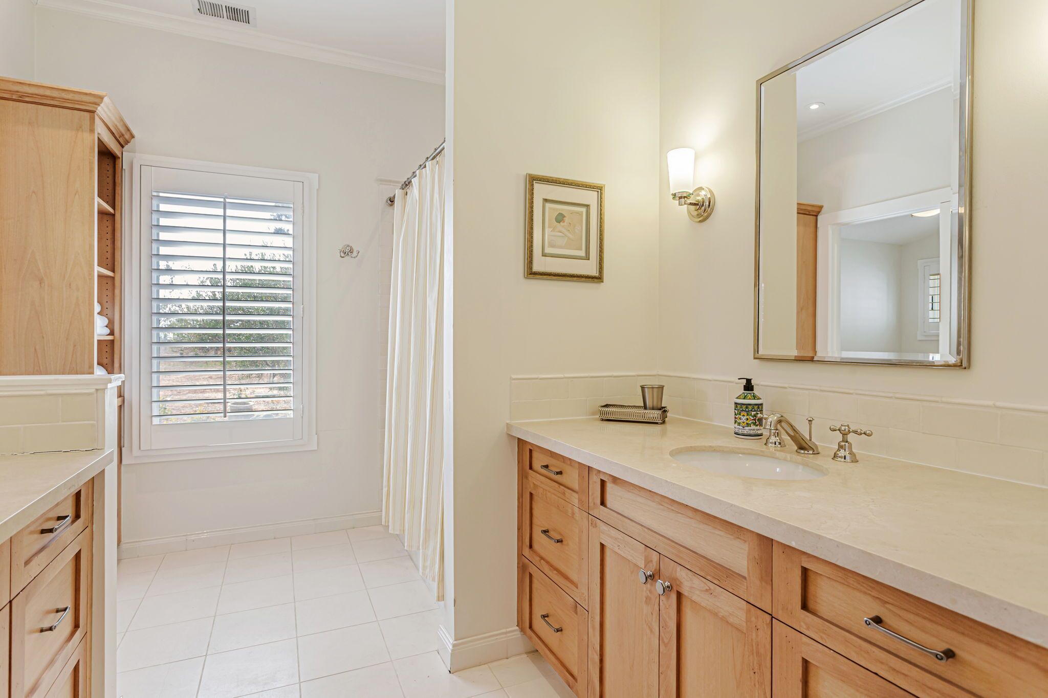 A bathroom with a large mirror, wooden cabinets, a sink, and a shower curtain.