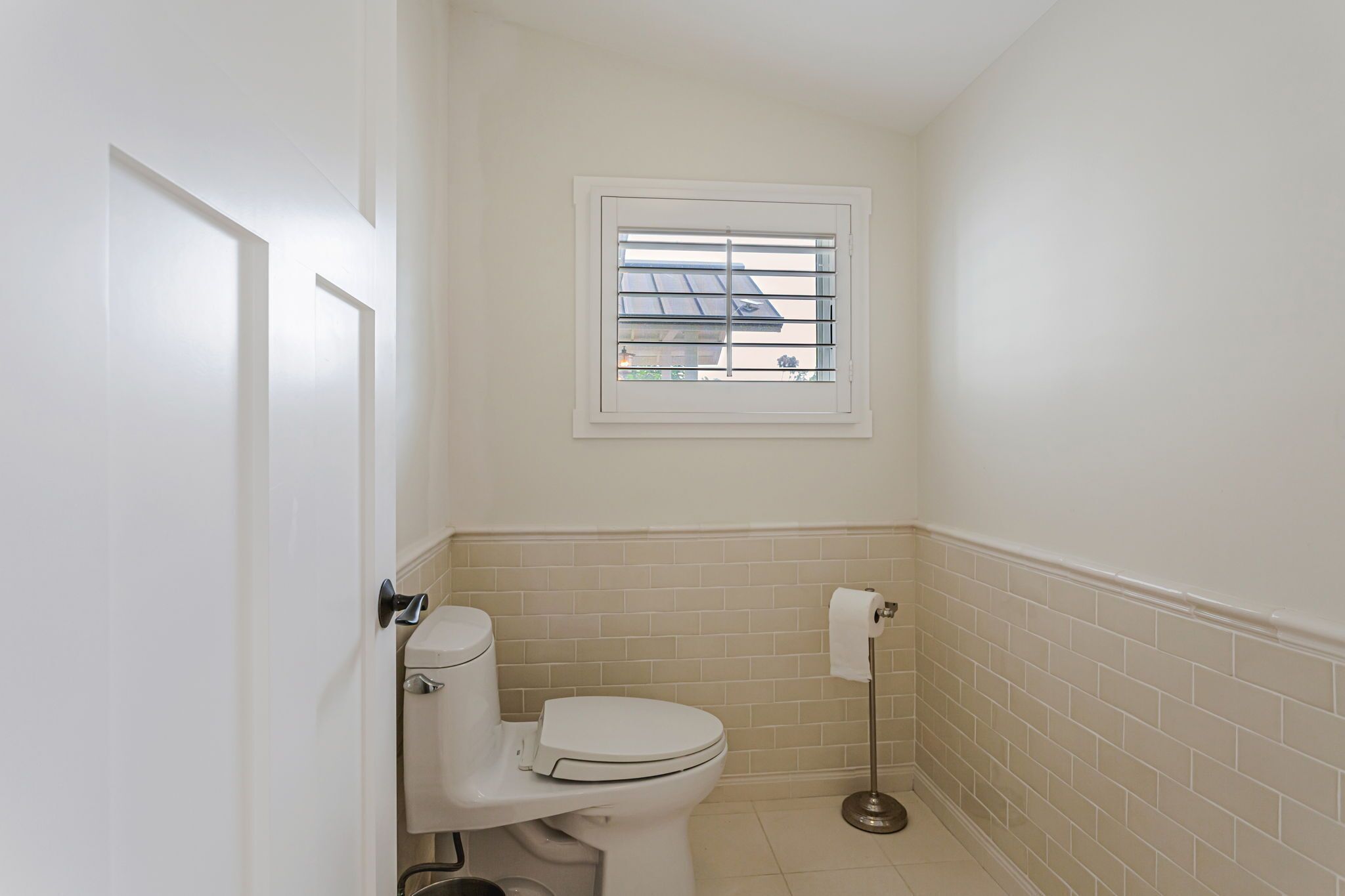 Un baño pequeño y limpio con inodoro, ventana y dispensador de papel higiénico.