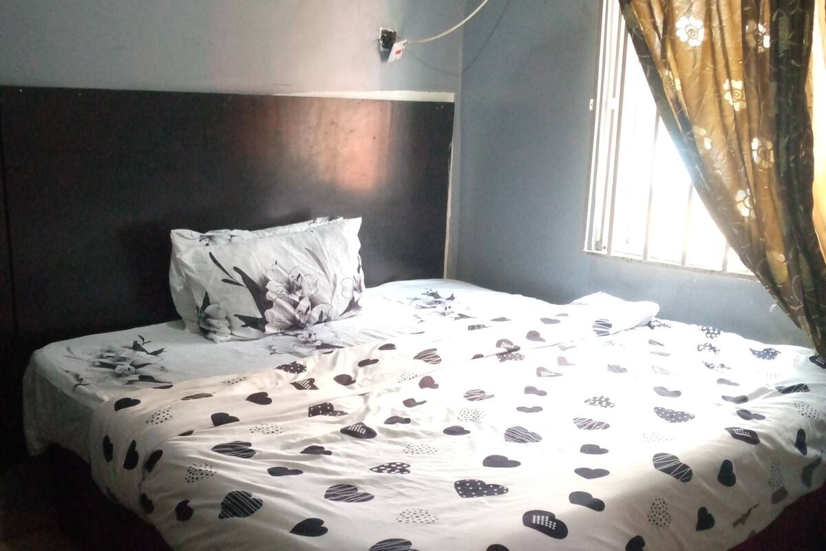 Un lit avec une couvre-lit à motifs de cœurs, un oreiller à motifs floraux et une fenêtre avec un rideau.