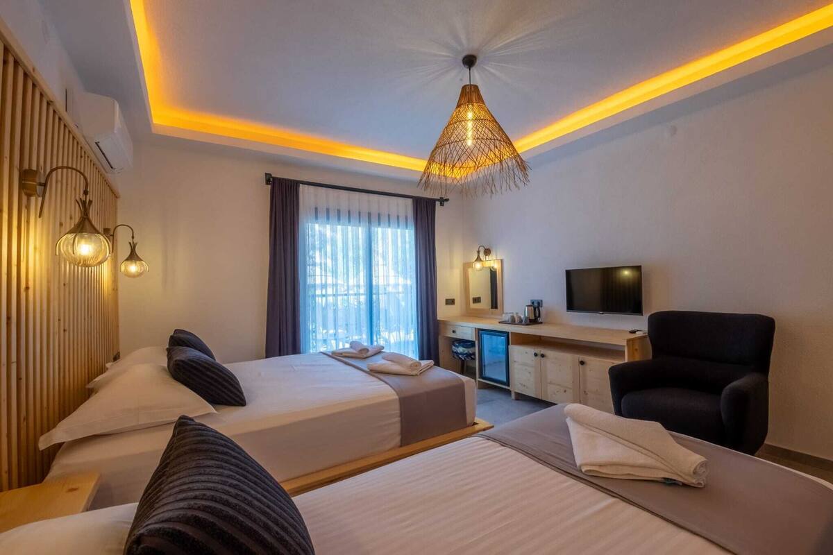 Une chambre d’hôtel avec deux lits, un bureau, une chaise, une télévision et une grande fenêtre avec des rideaux.