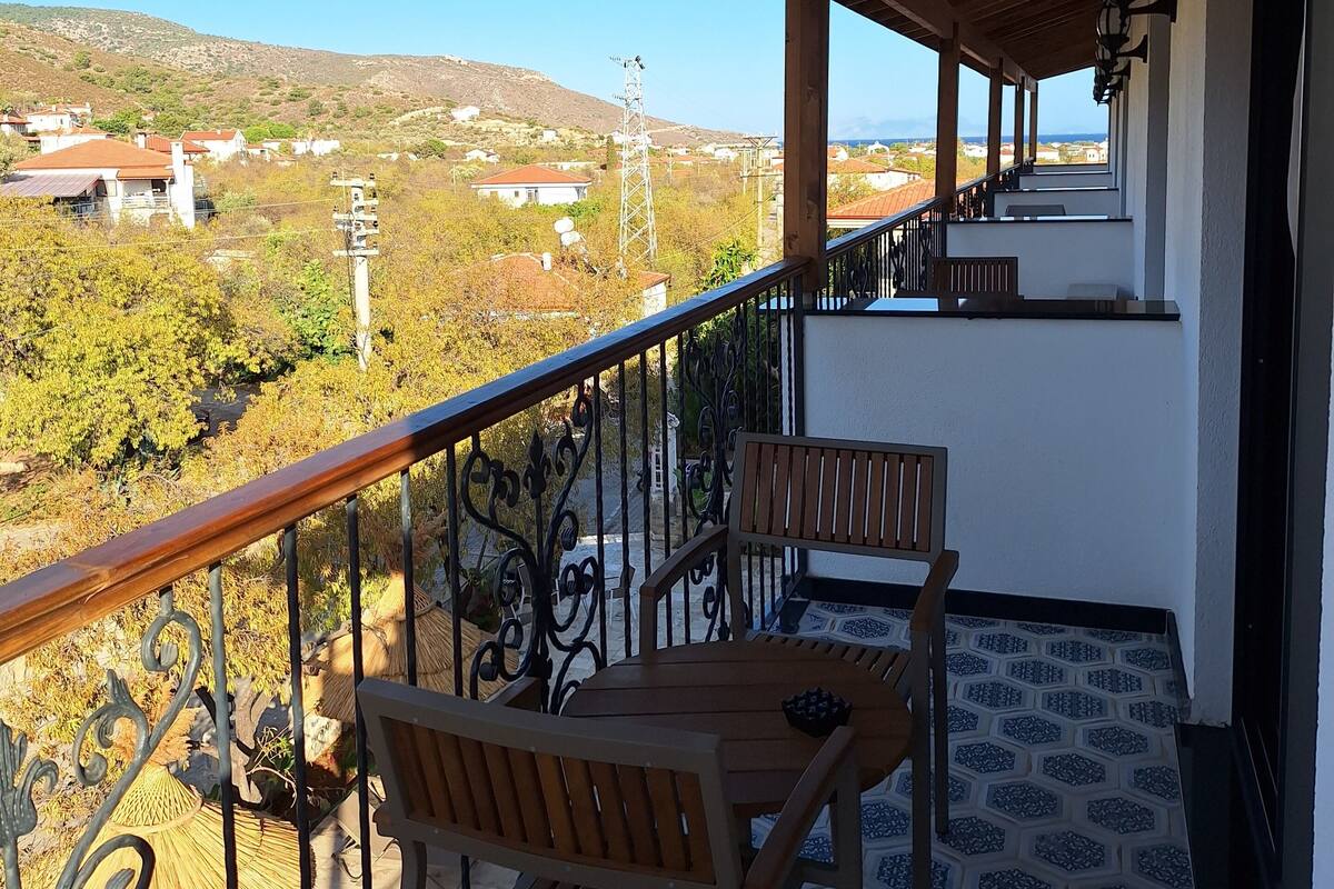 Un balcon avec une table et des chaises en bois, un sol à motifs et une vue sur un paysage vallonné.