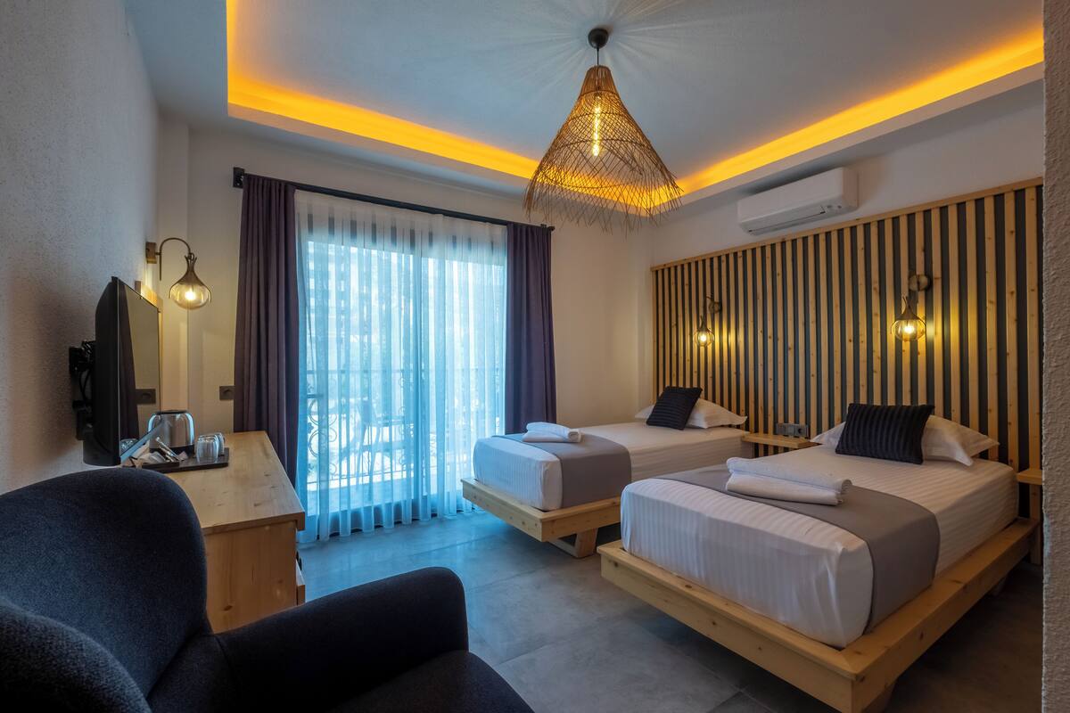 Une chambre d’hôtel moderne équipée de deux lits, d’un bureau, d’une chaise et d’une grande fenêtre avec des rideaux.